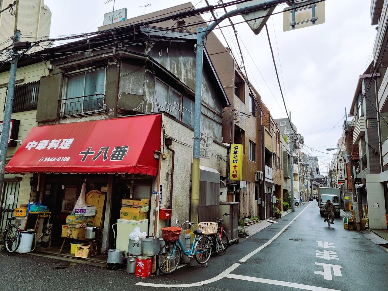 Rustic Japanese street scene featuring a traditional storefront with red awning and bicycles.